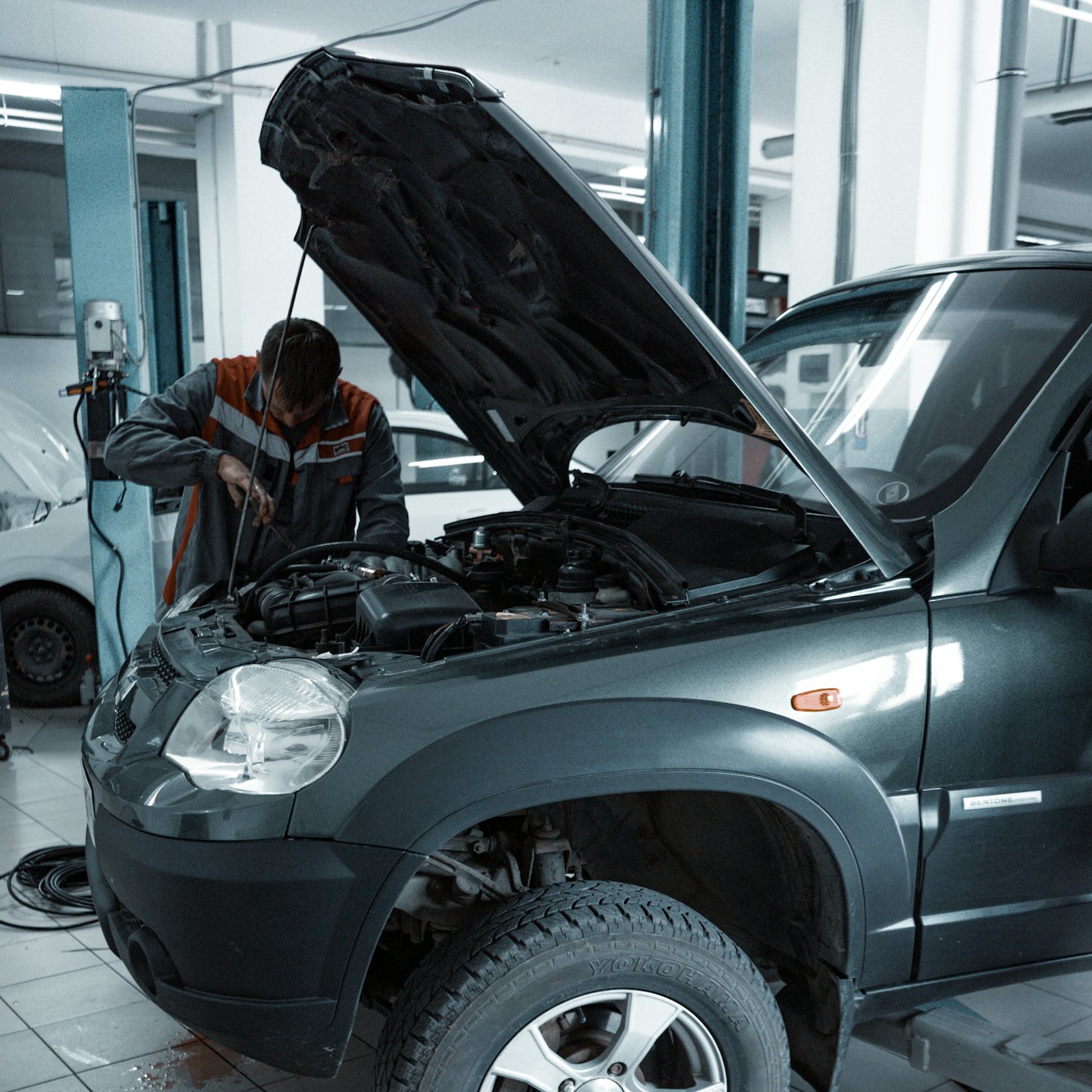 Mechanic in uniform repairs SUV engine in auto shop.