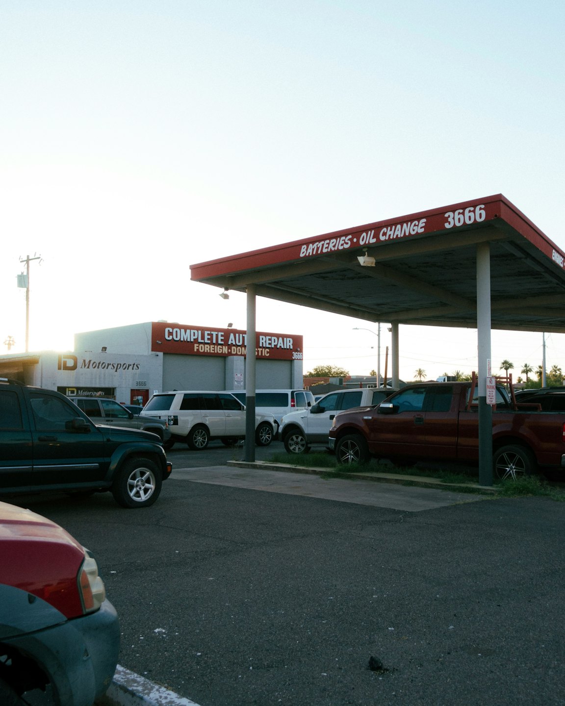 Auto repair shop with vehicles parked under red overhang.